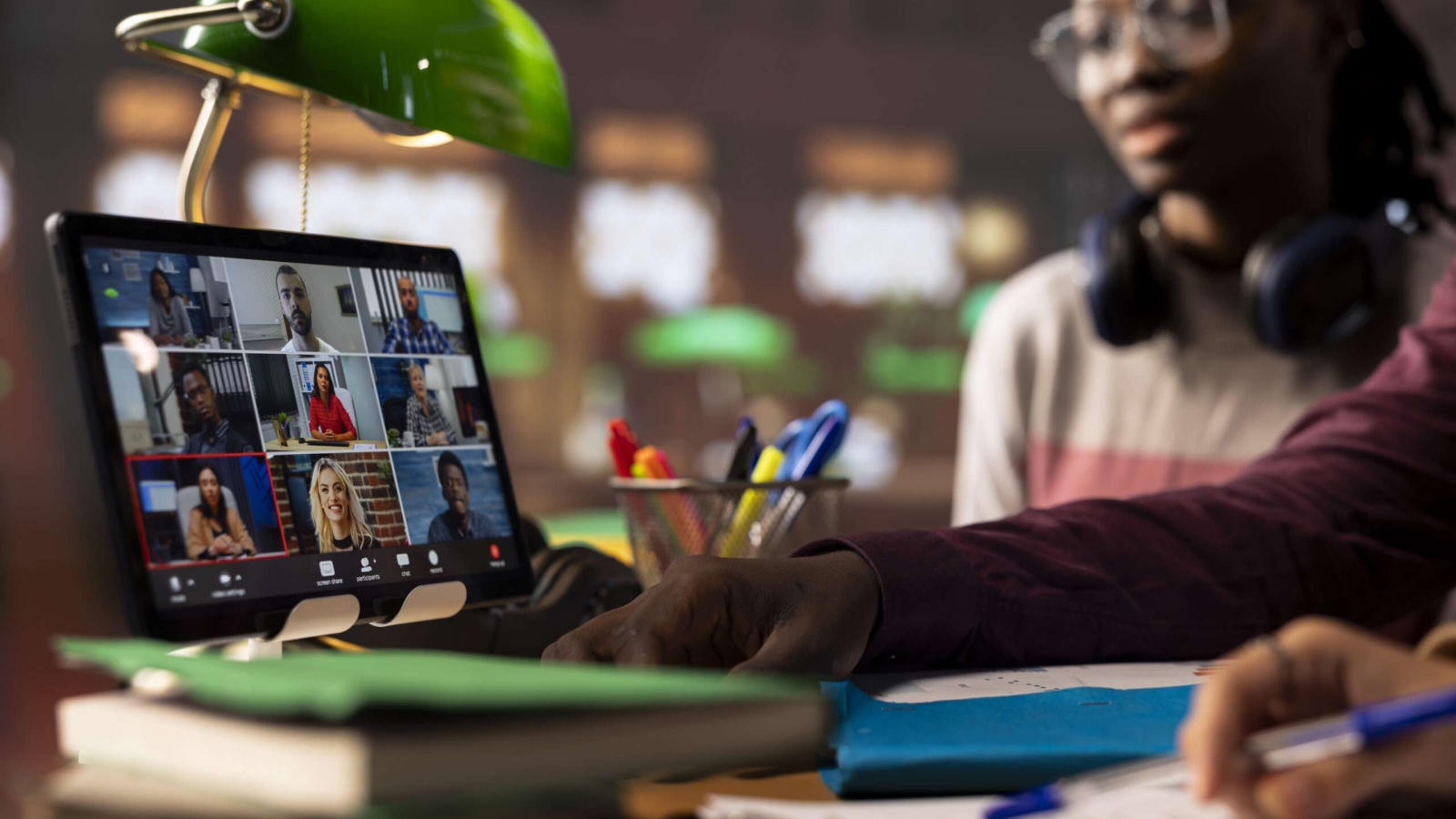 Group of diverse pupils engaging in an online course discussion via video call, participating at the remote class seminar from the campus library. Young people takes notes from academic tutor.