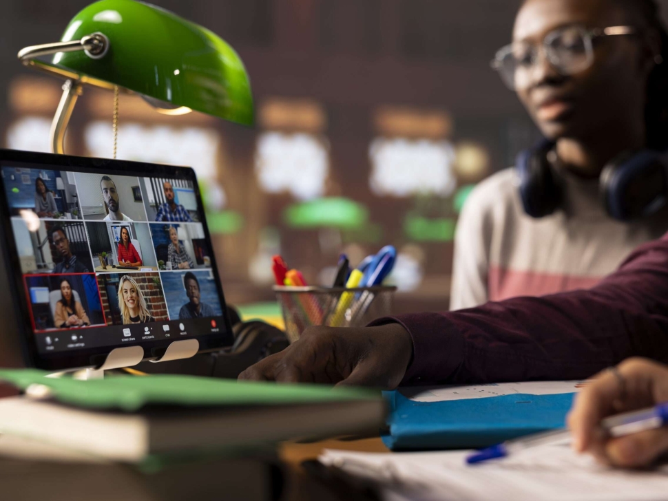 Group of diverse pupils engaging in an online course discussion via video call, participating at the remote class seminar from the campus library. Young people takes notes from academic tutor.